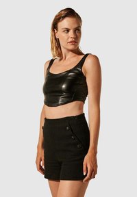 Haut court en similicuir noir avec encolure carrée, associé à un short noir texturé taille haute avec des accents de boutons.