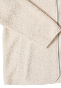 Veste en polaire sherpa couleur crème avec manche visible, poche avant, bouton-pression et fermeture éclair partielle sur le côté droit.