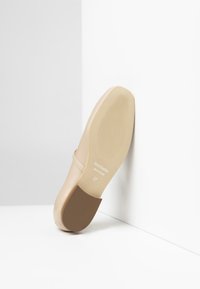 Chaussure pour femme beige avec une tige en cuir lisse et une semelle en caoutchouc marron contrastante. Présente un design plat et un marquage de taille 37.