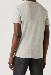 Camiseta de algodón gris con cuello redondo, mangas cortas y un ajuste holgado. Incluye una etiqueta en el dobladillo y tiene una textura suave.