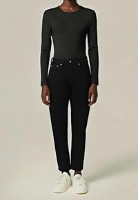 Vaqueros negros de talle alto con un corte entallado y una ligera reducción, combinados con una camiseta de manga larga oscura y zapatillas blancas.