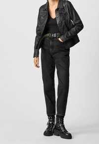 Schwarze Lederjacke über einem schwarzen gerippten Oberteil, kombiniert mit schwarzen, hoch taillierten Jeans und schwarzen Kampfstiefeln mit silberner Hardware.