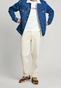 Denimjacka med sherpa-krage, vit t-shirt med röd text, beige byxor och bruna/svarta sportiga sneakers. Avslappnad outfit med lager av olika texturer.