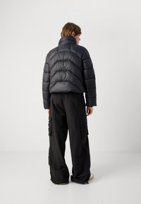 Casaco puffer preto com colarinho alto e costura horizontal, combinado com calças cargo pretas largas com bolsos laterais.