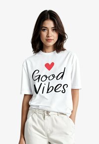 Witte katoenen T-shirt met "Good Vibes" in vette zwarte letters en een rode hart, korte mouwen en een losse pasvorm.