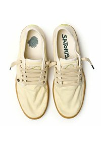 Zapatillas de lona beige con cordones redondos, suelas de goma y acentos verdes. Presenta un logo con un gráfico de león en la plantilla.