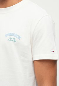 Tricou alb din bumbac, cu text brodat în nuanțe de albastru deschis și verde "TOMMY JEANS New York City" pe piept; logo mic pe mânecă.