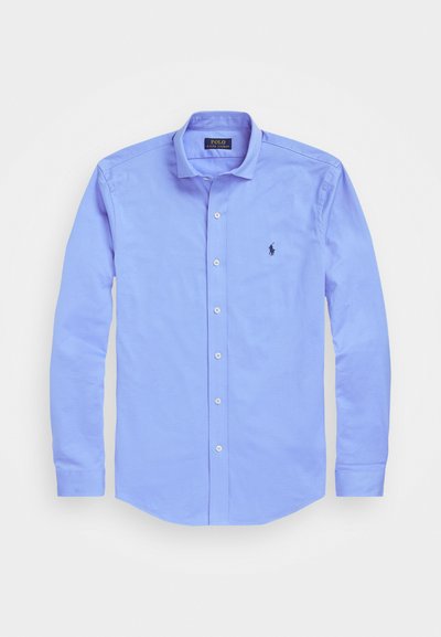 Gaiši zils pogām krekls, kas izgatavots no kokvilnas. Iezīmē klasisku apkakli, garām piedurknēm un nelielu logo izšuvumu kreisajā krūtī.