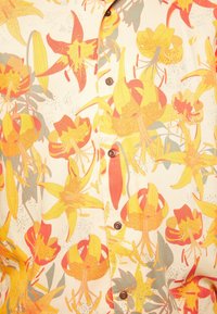 Camicia a maniche corte con motivo floreale, caratterizzata da uno sfondo crema con grandi fiori di giglio gialli, rossi e verdi e bottoni marroni.
