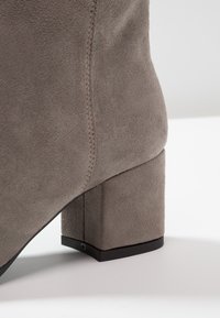 Stivale alla caviglia in suede grigio con tacco a blocco, linee pulite e cuciture a vista lungo il lato per un tocco di dettaglio. Texture opaca in tutta la superficie.