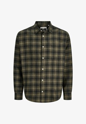 Zöld kockás flaneling fehér grafikás póló felett, lazán szabott, sötétszürke farmernadrággal és bézs lábbelivel, amely gumitalppal készült.