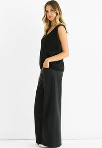 Black knitted sleeveless top with a V-neck and subtle shimmer, paired with wide-leg black denim trousers. Casual and relaxed fit.