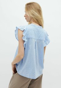 Blusa azzurro chiaro con maniche a balze, tessuto testurizzato e vestibilità rilassata. Presenta un retro plissettato e sottili righe verticali.