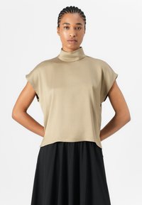 Top beige con colletto alto e maniche corte. Tessuto liscio e vestibilità rilassata, abbinato a una gonna nera fluida per un contrasto.