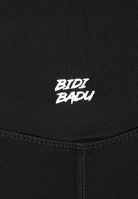 Tejido de activewear negro con una superficie texturizada y el logo blanco "BIDI BADU" destacado cerca del dobladillo.