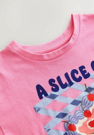 T-shirt en coton rose avec un col rond et un design graphique d'un dessert avec des cerises, superposé sur un fond carreauté bleu et blanc.