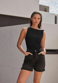 Top negro sin mangas con detalle fruncido en el hombro, combinado con pantalones cortos de mezclilla oscura de cintura alta y dobladillo enrollado. Tela suave y diseño ajustado.