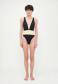 Svart baddräkt i ett stycke med djup V-ringning och bred gul midjesjal. Slät tyg, minimalistisk design och högskurna ben.