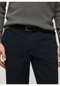 Marineblaue Hose mit glatter Textur, flachem Vorderteil, Gürtelschlaufen und schmaler Passform, kombiniert mit einem grauen Strickpullover.