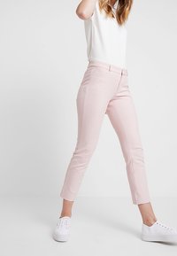 Pink, tailored pants with a subtle ribbed texture, tapered legs, and a mid-rise waist. Paired with a white top and white sneakers.
