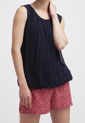 Mouwloos marineblauw topje met geplooid ontwerp, gecombineerd met rode korte broek met een klein wit bloemmotief. Gladde stof en een comfortabele pasvorm.