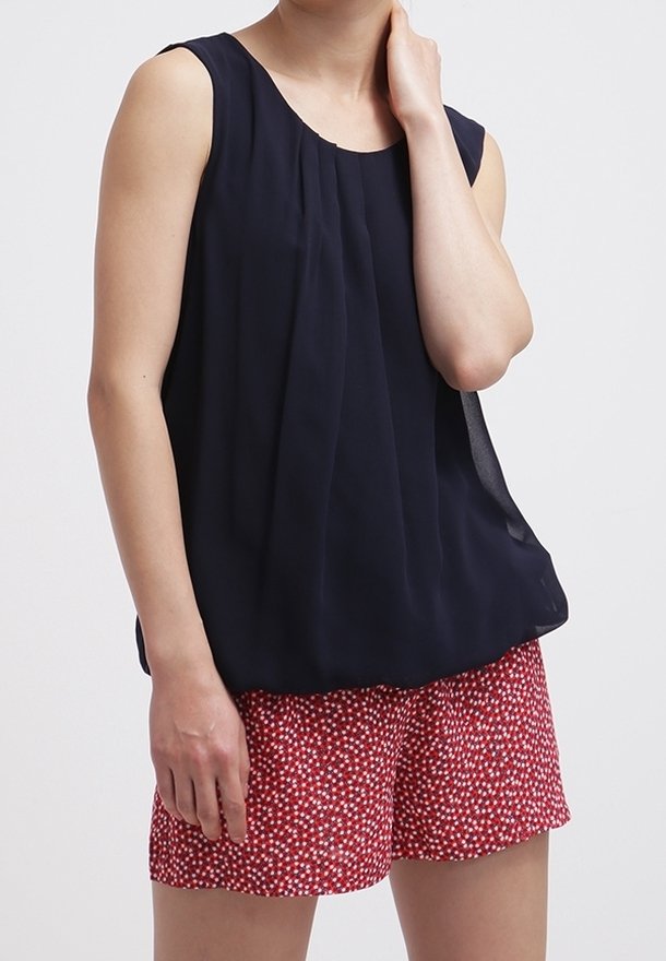 Haut sans manches bleu marine avec un design plissé, assorti à un short rouge orné d'un petit motif floral blanc. Tissu lisse et coupe décontractée.