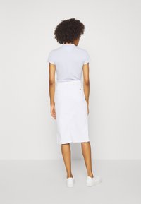 Camiseta de manga corta azul claro combinada con una falda midi de mezclilla blanca. La falda cuenta con una cintura con cinturón y dos bolsillos traseros. Zapatillas blancas completan el look.
