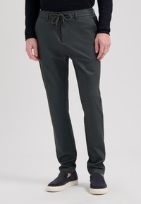 Mørkegrønne, elastiske bukser med snøre i taljen. Glat tekstur, tapered fit, frontlommer. Kombineret med marineblå slip-on sko.