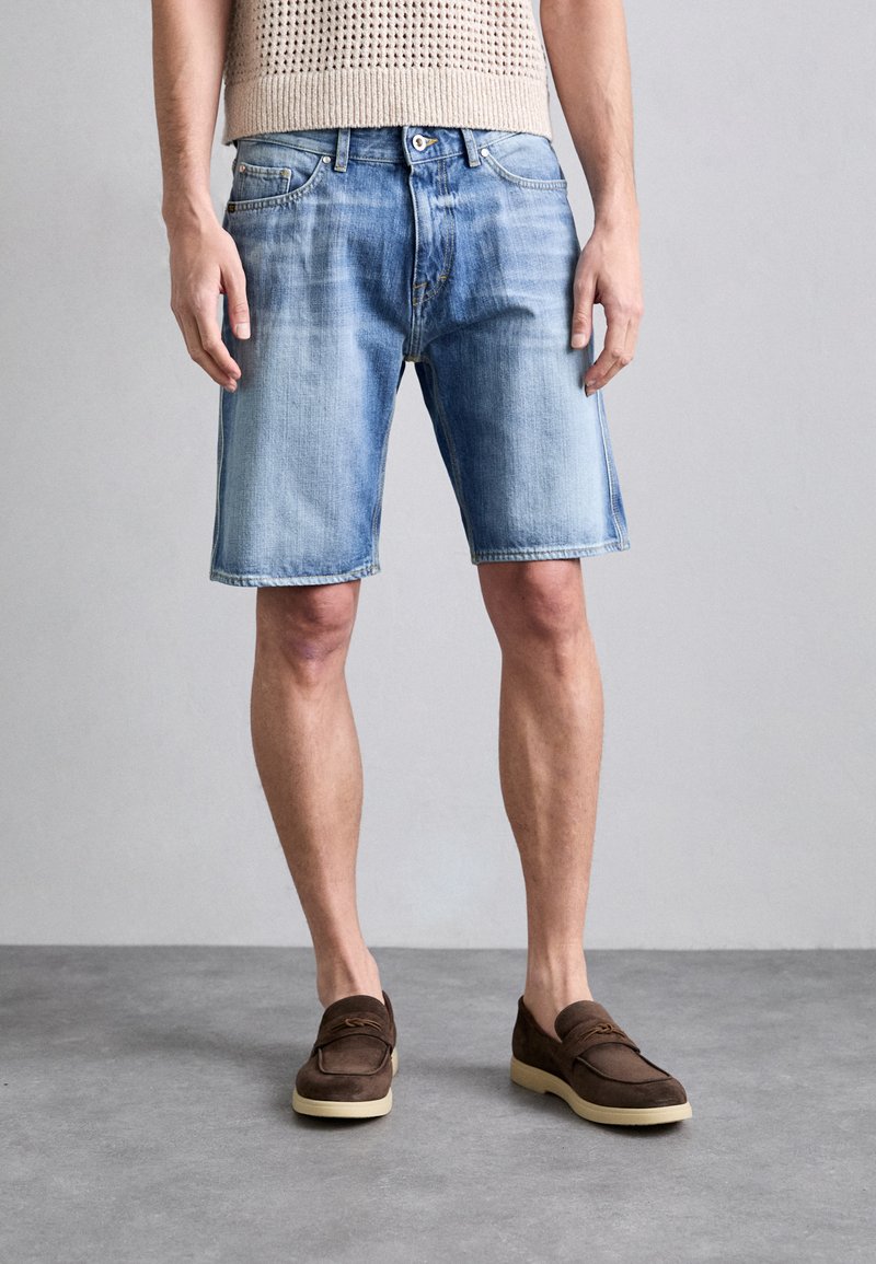 Șorturi din denim, de culoare albastru deschis cu umbre, cinci buzunare și detalii cu cuie metalice. Asortate cu mocasini din suede maro.