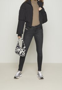 Chaqueta de plumas negra, suéter de cuello alto beige, jeans ajustados oscuros, zapatillas plateadas y un bolso negro y blanco con estampado. Conjunto simple y funcional.