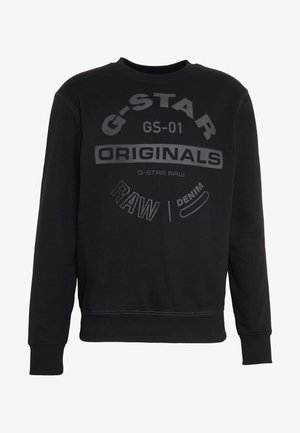 Černá mikina s dlouhým rukávem s žebrovanými manžetami a spodním lemem, s textem "G-STAR ORIGINALS RAW DENIM" tištěným různými fonty přes hrudník.