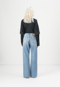 Jeanși largi de culoare bleu deschis cu talie înaltă, buzunare la spate și un eticheta de brand din piele maro. Asortați cu un tricou negru supradimensionat.