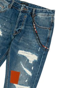 Vaqueros de mezclilla de tela azul claro desgastada, con un parche marrón, cadena con cuentas y manchas de pintura en la superficie.