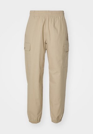 Pantalons cargo beiges avec une taille élastique, des jambes effilées et des poches latérales. Tissu lisse avec une texture légèrement structurée.