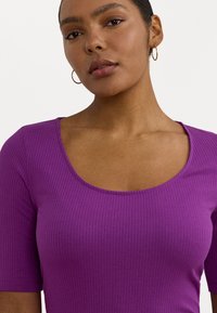 Top viola a costine con scollatura a barchetta e maniche corte, caratterizzato da una superficie liscia e una forma aderente.