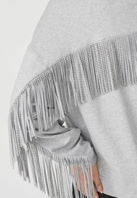 Grau Sweatshirt mit einem breiten Fransendesign, das am oberen Rand mit metallischen Nieten akzentuiert ist, aus weichem Stoff und mit lockerer Passform.