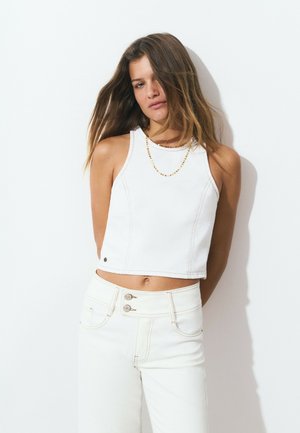 Top corto blanco sin mangas con costuras en contraste, combinado con jeans blancos de tiro alto con cierre de dos botones y bolsillos laterales.