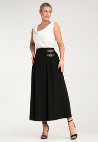 Czarna plisowana spódnica z brązowymi akcentami podwójnego zapięcia, w połączeniu z białą bluzką z dekoltem typu cowl. Posiada zwiewny fason i gładką teksturę.
