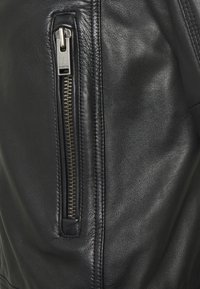 Svart läderjacka med en vertikal metallblixtlås där "SELECTED" är ingraverat på dragfliken.