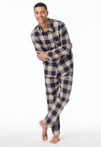 Pigiama a quadri in beige, blu navy e grigio. Maglia a maniche lunghe con tasca; pantaloni abbinati. Tessuto morbido, vestibilità comoda, piedi nudi visibili.