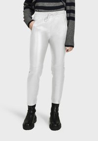 Witte, glanzende, strakke broeken met een trekkoord in de taille en zijzakken, gecombineerd met zwarte leren enkellaarsjes en een gestreepte trui.