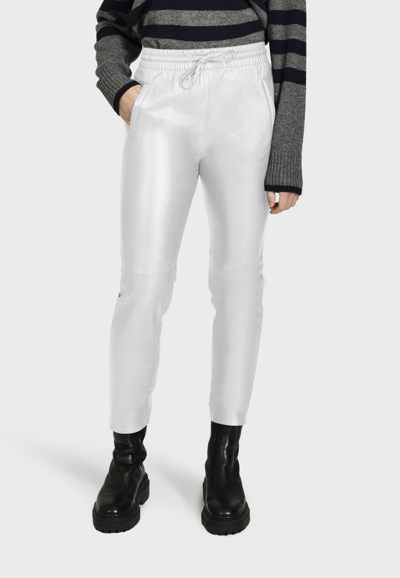 Witte, glanzende, strakke broeken met een trekkoord in de taille en zijzakken, gecombineerd met zwarte leren enkellaarsjes en een gestreepte trui.