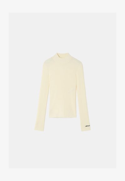 Ribbed, long-sleeve turtleneck top in light yellow, featuring a fitted design and black accent text on the cuff. Soft fabric texture.
