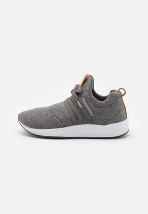 Grå slip-on sneaker med elastiske snørebånd, hvid sål og brune trækflige på hæl og tunge, vist på en ensfarvet baggrund.