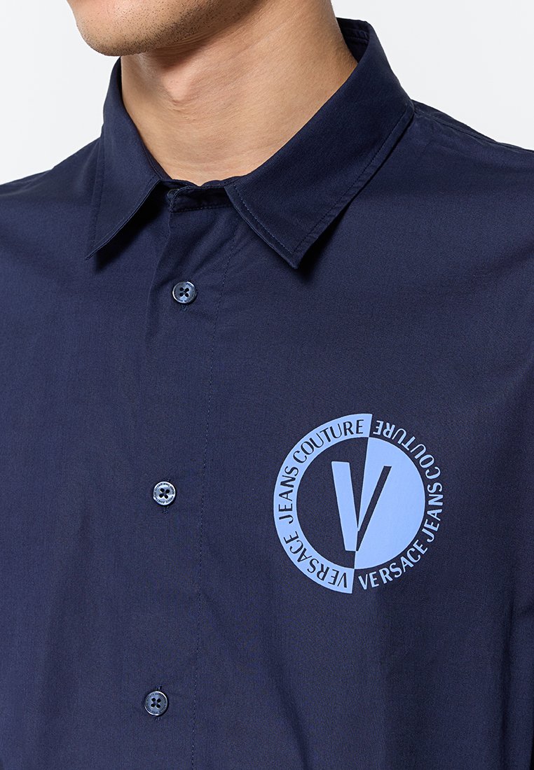 Chemise boutonnée bleu marine avec col écarté, ornée d'une impression de logo bleue sur la poitrine gauche et de boutons assortis sur le plastron.