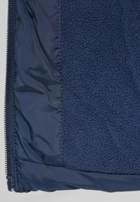 Navyblauwe jas met een contrasterende gladde en textuurstof, gemaakt van fleece en nylon materialen, en een volle rits.