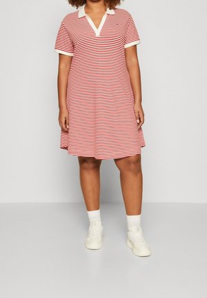 Osoba ubrana w czerwoną i białą pasiastą sukienkę polo o długości do kolan z białym kołnierzykiem i mankietami, białe skarpetki oraz białe tenisówki.