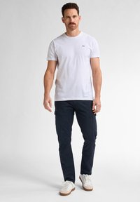 Hvid bomulds T-shirt med et lille sort logo. Blandet med marineblå cargo bukser med sidelommer. Skoene er hvide med brune accenter.
