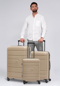 Tres maletas rígidas beige de diferentes tamaños; superficie texturizada con surcos horizontales, asas retráctiles y ruedas giratorias.