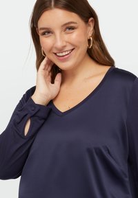 Marineblauwe V-hals blouse van soepel stof met lange mouwen, voorzien van knoopaccenten en een splitdetail bij de manchetten.